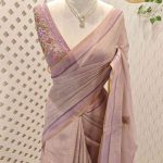 Linen saree with a border is adorned with detailed floral embroidery, possibly using French knots, and features sequins and a decorative woven edge